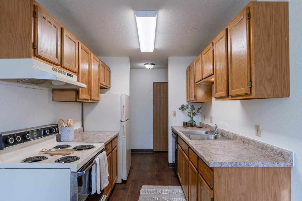 a kitchen with wood cabinets and white appliances and a counter top. Fargo, ND Place One Apartments