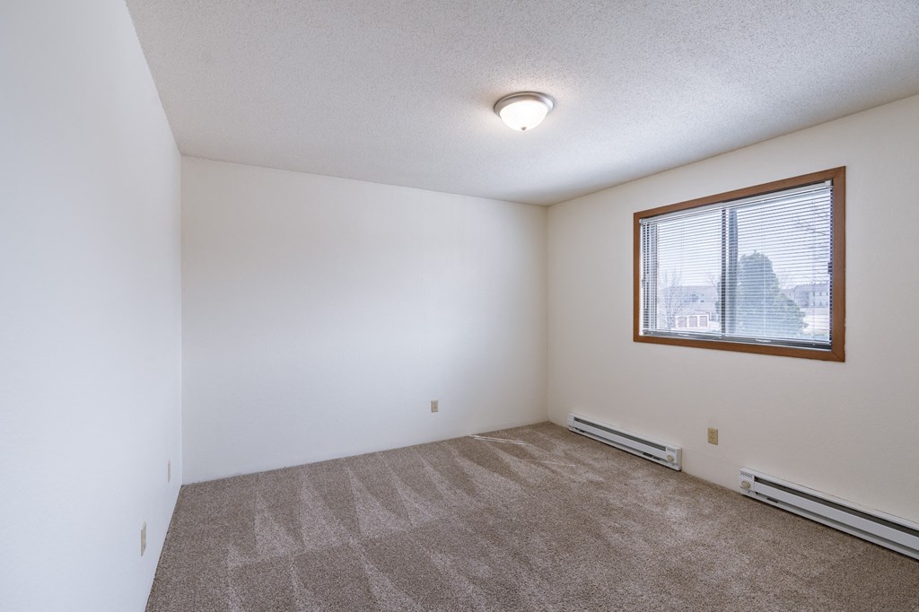 a bedroom of an apartment with carpet and a window. Fargo, ND Place One Apartments
