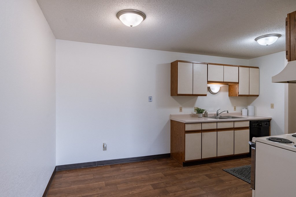 an empty kitchen with white walls and wood flooring and a sink and a counter. Fargo, ND Place One Apartments