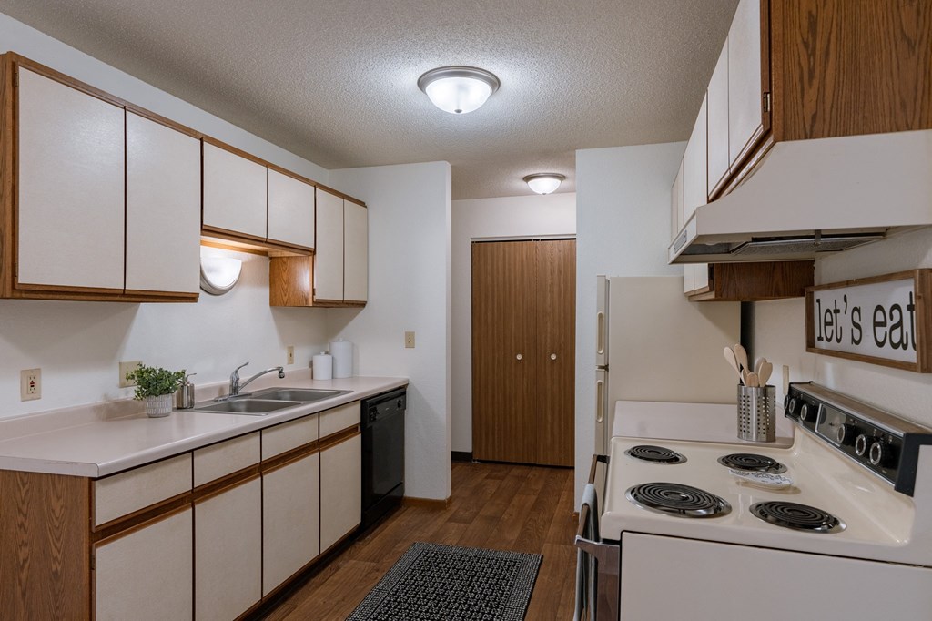 a kitchen with white appliances and wooden cabinets and a stove top oven. Fargo, ND Place One Apartments