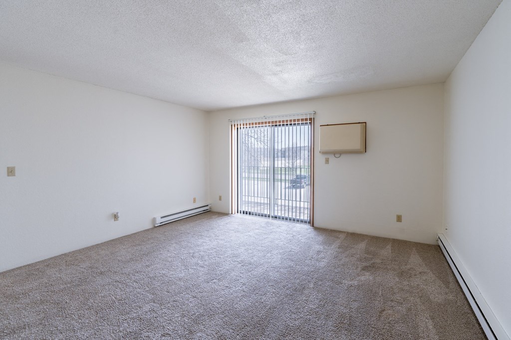 an empty living room with a sliding glass door and carpeted floor. Fargo, ND Place One Apartments
