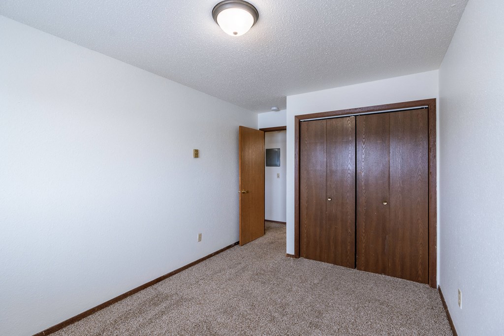 a bedroom with carpet and a door to a closet. Fargo, ND Plumtree Apartments