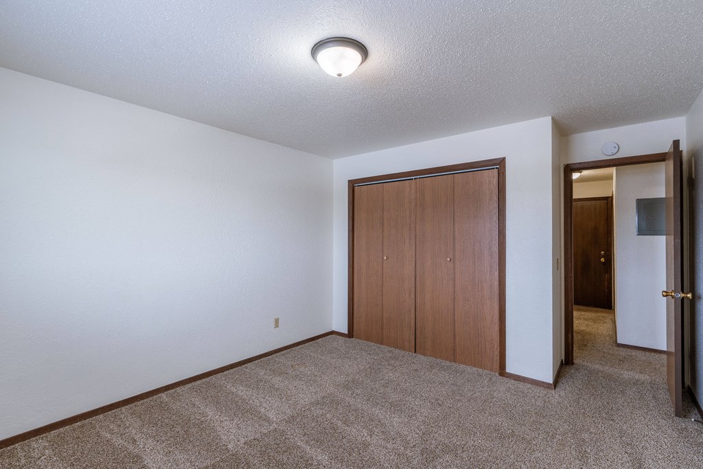 a room with a carpeted floor and a door to a hallway. Fargo, ND Plumtree Apartments