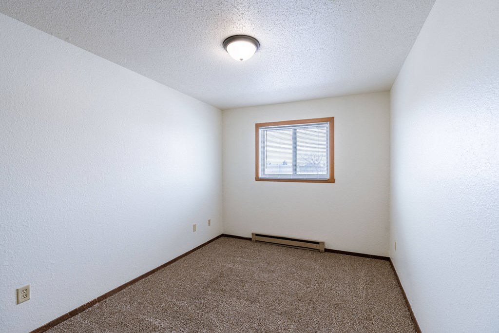 a bedroom of an empty house with carpet and a window. Fargo, ND Plumtree Apartments