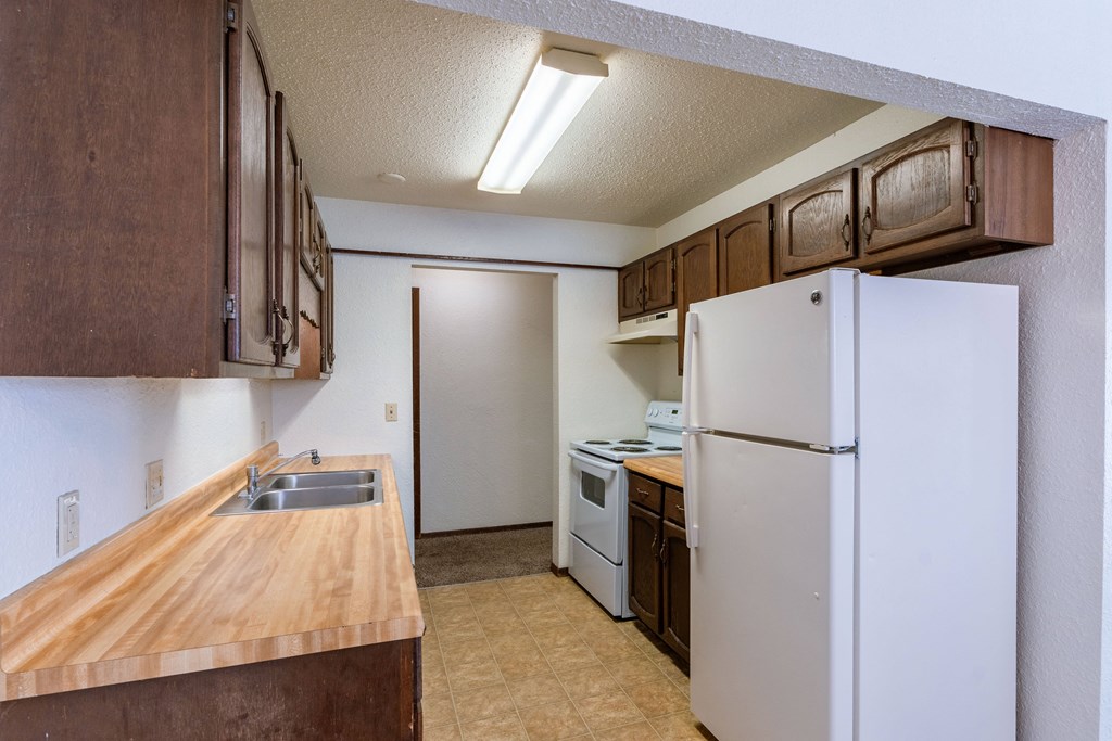 an empty kitchen with a refrigerator and a sink. Fargo, ND Plumtree Apartments