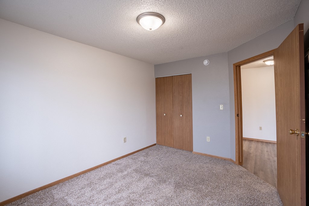 a bedroom with a door to a closet and a carpeted floor. Fargo, ND  Prairie Park Apartments