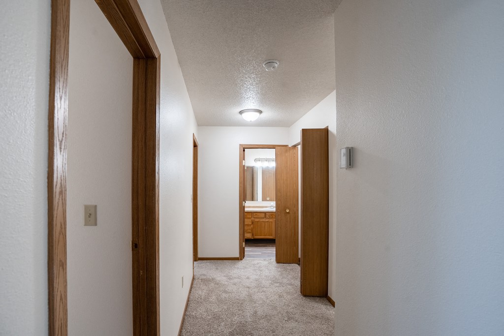 a hallway with a carpeted floor and wooden doors to a bathroom. Fargo, ND  Prairie Park Apartments
