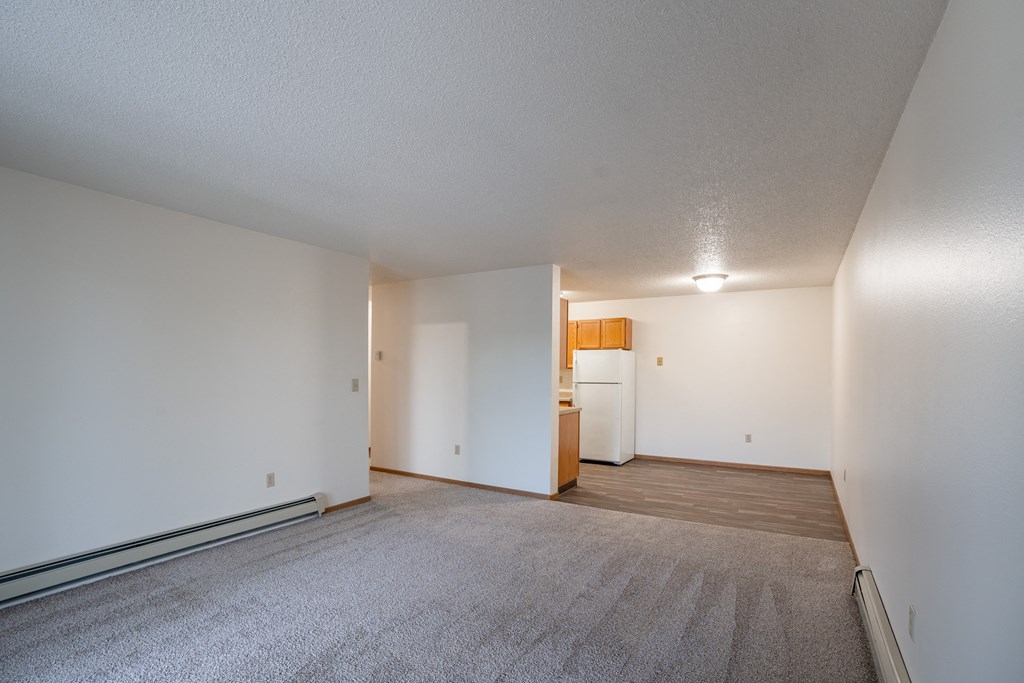 the living room and kitchen of an apartment with white walls and carpet. Fargo, ND  Prairie Park Apartments