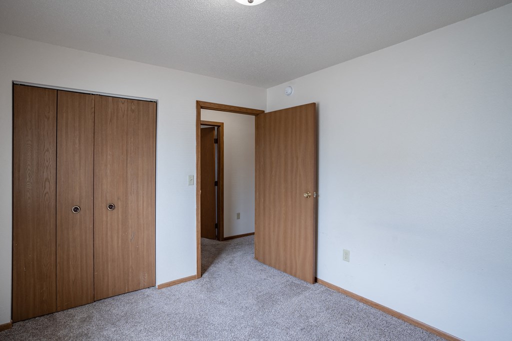a bedroom with two closet doors and a door to a hallway. Fargo, ND  Prairie Park Apartments