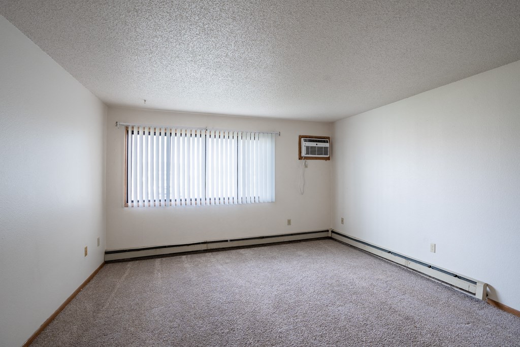 the living room of an empty house with white walls and a window. Fargo, ND  Prairie Park Apartments