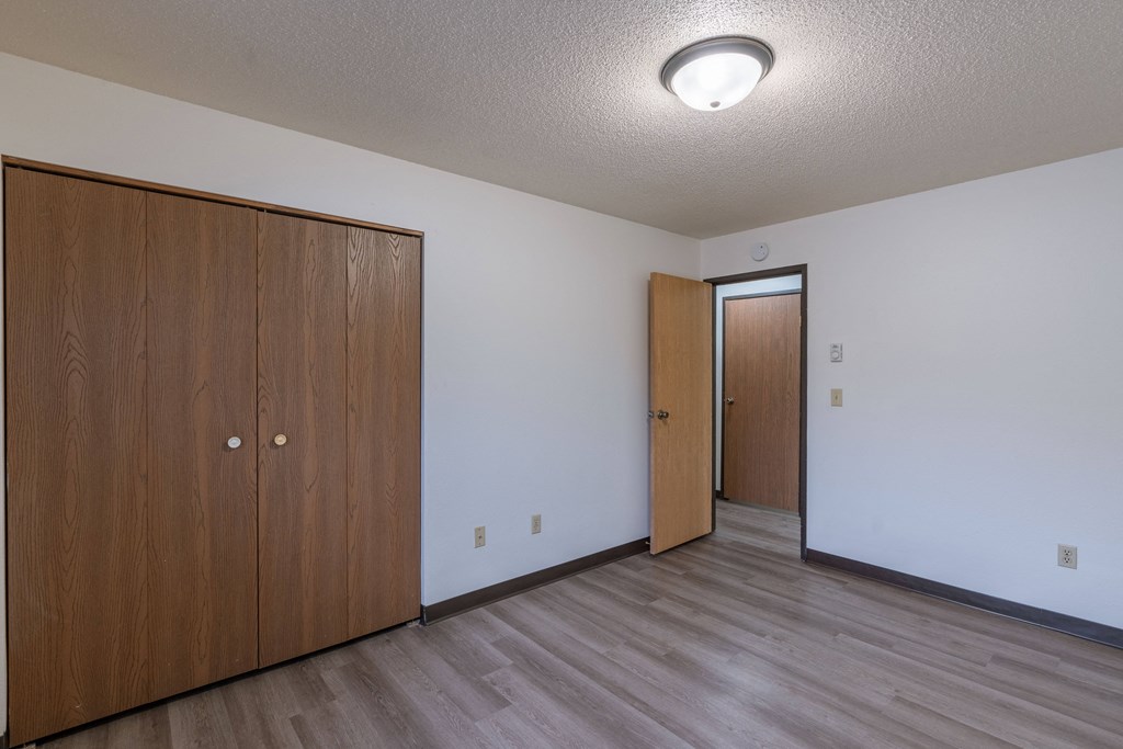 a bedroom of an apartment with a door to the hallway and a closet. Fargo, ND Prairiewood Courts Apartments