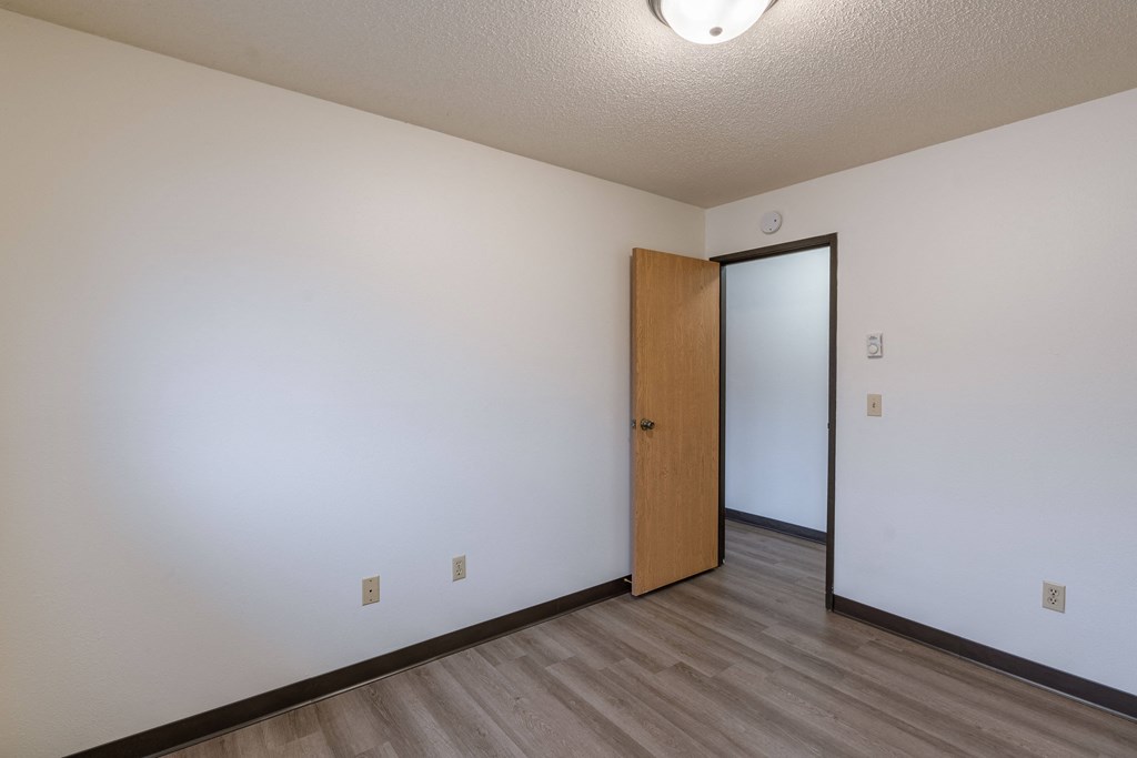 the living room of an empty apartment with a door to the hallway. Fargo, ND Prairiewood Courts Apartments