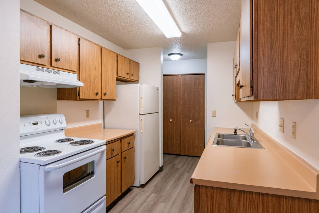 a kitchen with white appliances and wooden cabinets. Fargo, ND Prairiewood Courts Apartments