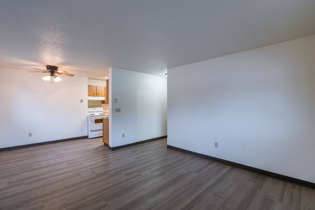 the living room and kitchen of an empty apartment with white walls and wood floors. Fargo, ND Prairiewood Courts Apartments