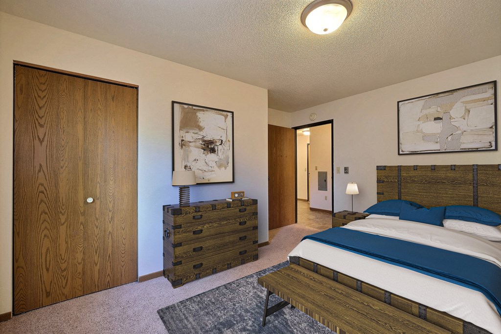 Fargo, ND Prairiewood Courts Apartments.  a bedroom with a bed and a dresser. A closet is in the corner of the room for extra storage.
