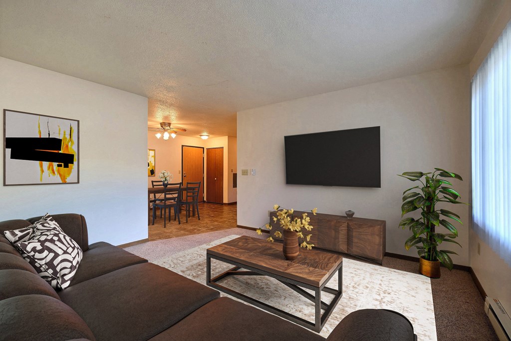 Fargo, ND Prairiewood Courts Apartments.  A living room with a couch, coffee table, and a tv. the dining room is in the background.