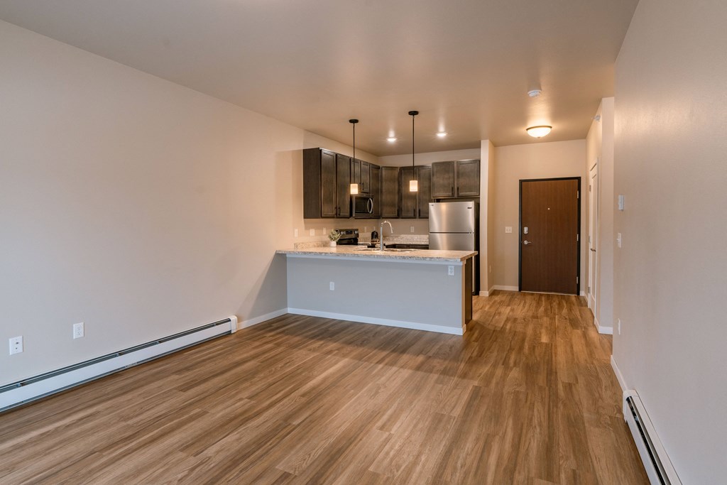 an empty living room with a kitchen with a sink and a refrigerator. Fargo, ND Prairiewood Meadows | LivingFargo, ND Prairiewood Meadows