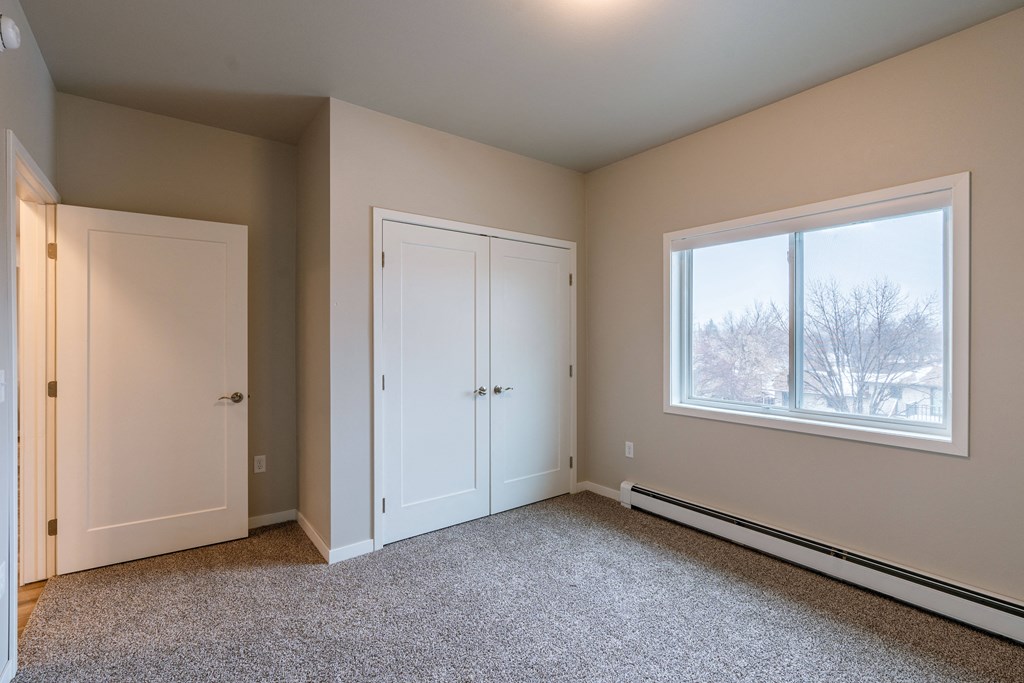 an empty bedroom with two doors and a window. Fargo, ND Prairiewood Meadows Apartments