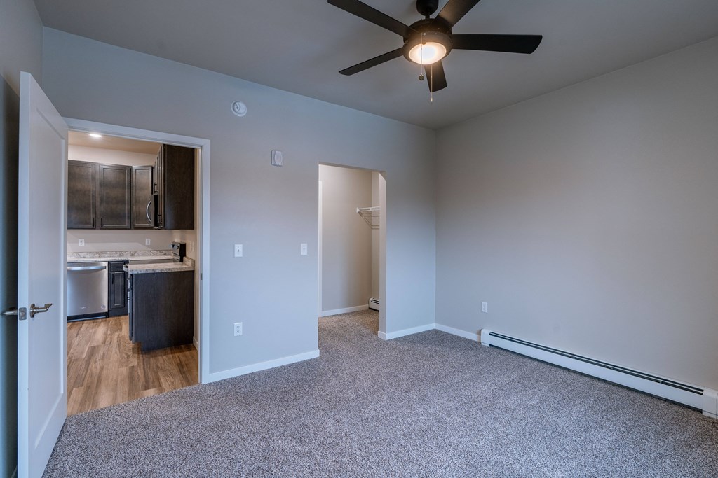 a bedroom with a ceiling fan and a kitchen. Fargo, ND Prairiewood Meadows Apartments