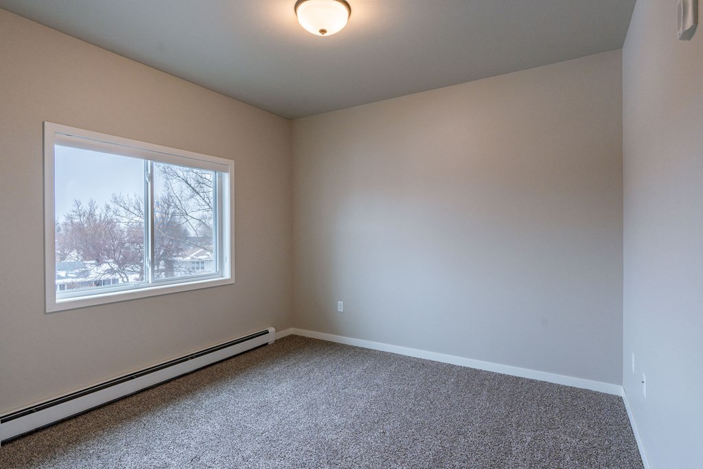 an empty room with carpet and a window. Fargo, ND Prairiewood Meadows Apartments