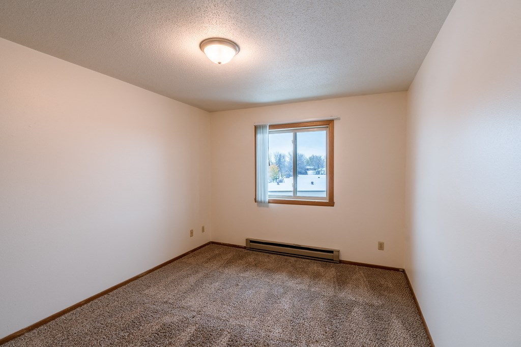 an empty living room with carpet and a window .Fargo, ND Sargent Apartments
