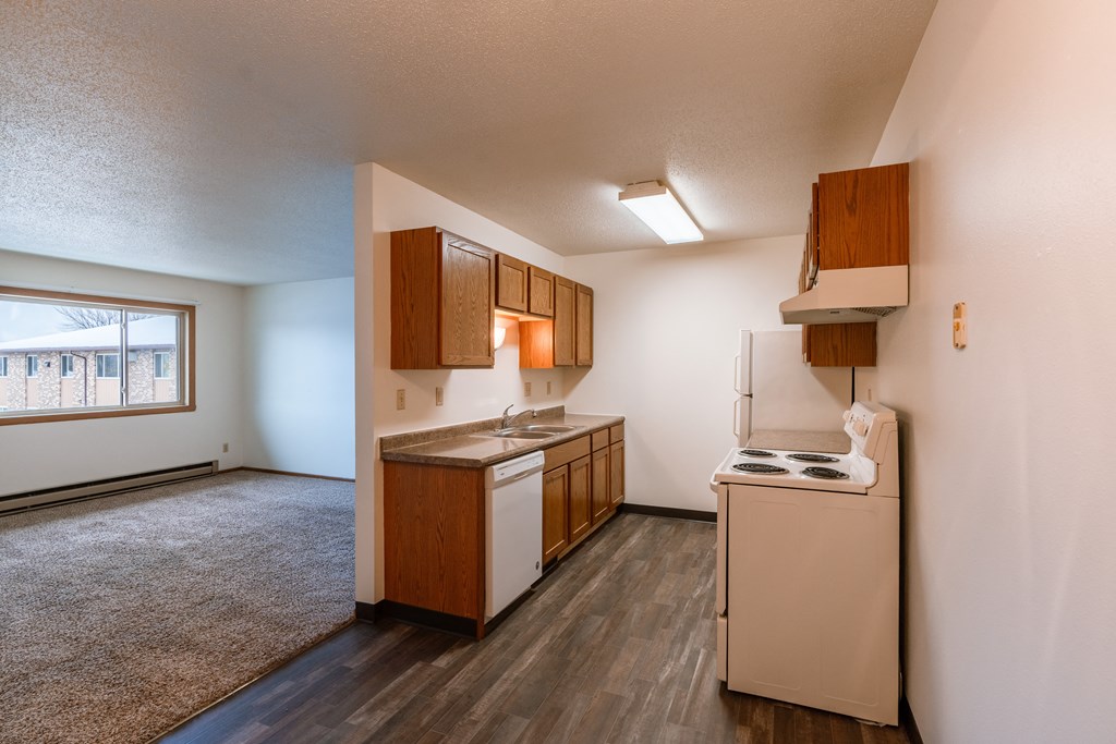 an empty kitchen with white appliances and wooden cabinets. Fargo, ND Sargent Apartments
