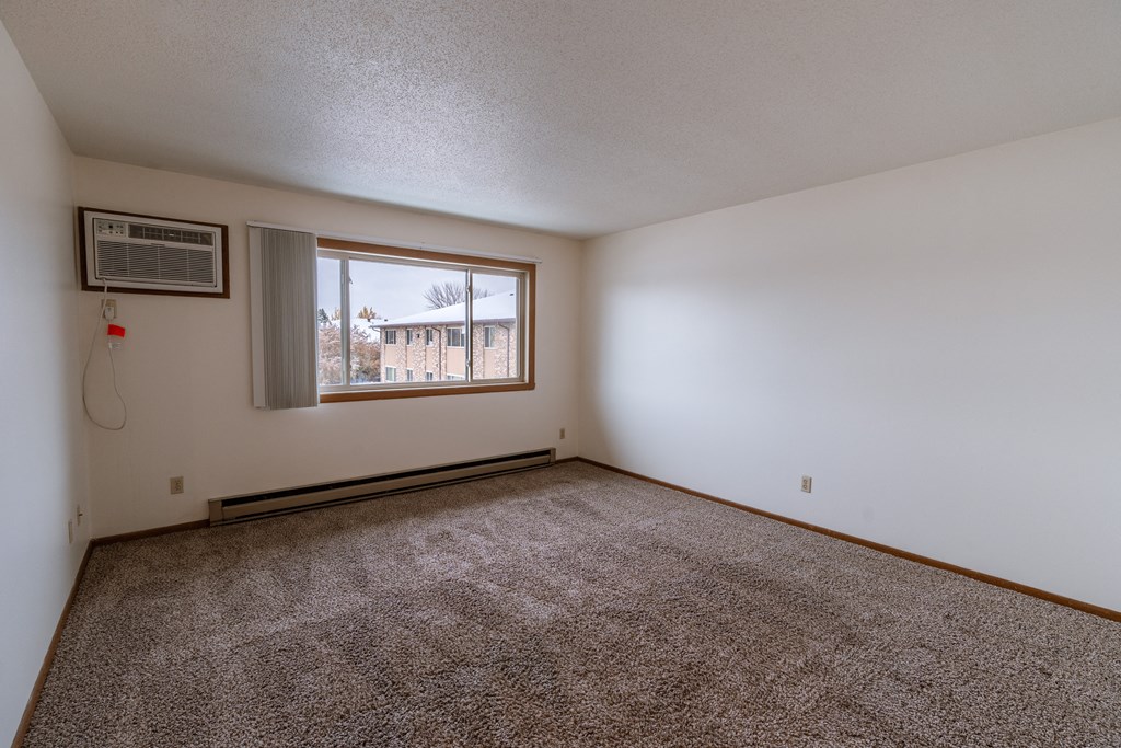 an empty living room with carpet and a window. Fargo, ND Sargent Apartments