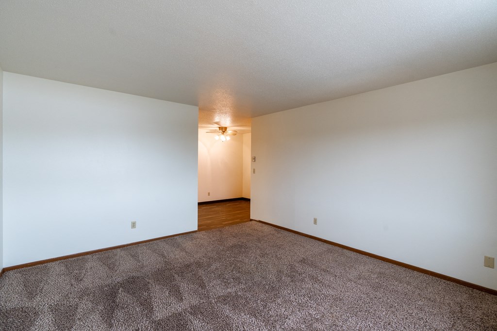 a spacious living room with carpet and white walls. Fargo, ND Sargent Apartments