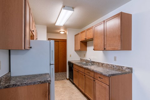 a kitchen with wood cabinets and granite counter tops and a refrigerator. Fargo, ND Schrock Apartments