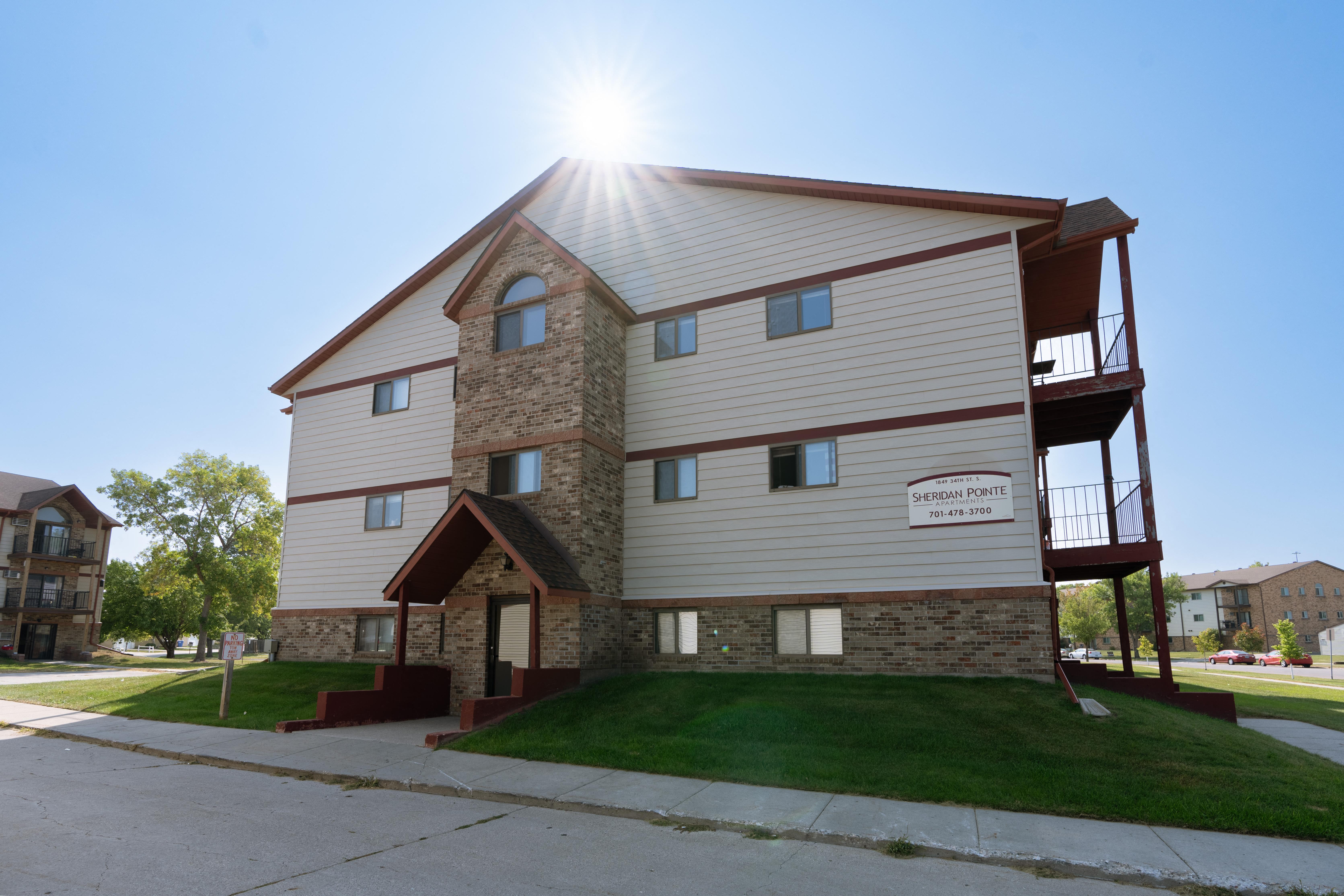 An exterior view of an apartment complex with a sidewalk in front of it. Fargo, ND Sheridan Pointe Apartments.