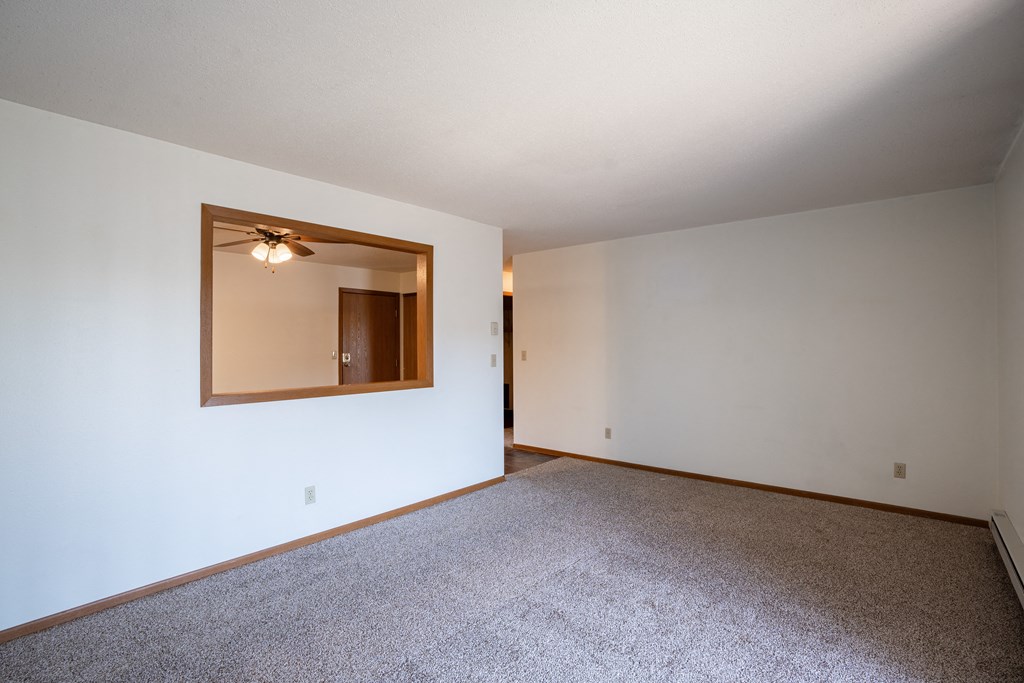 an empty living room with white walls and a large mirror. Fargo, ND Southview Village Apartments
