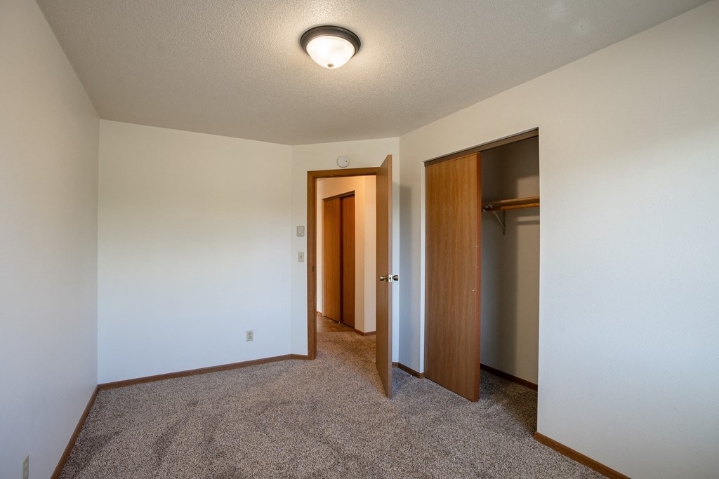 a bedroom with carpeted flooring and a door to a closet. Fargo, ND Southview Village Apartments