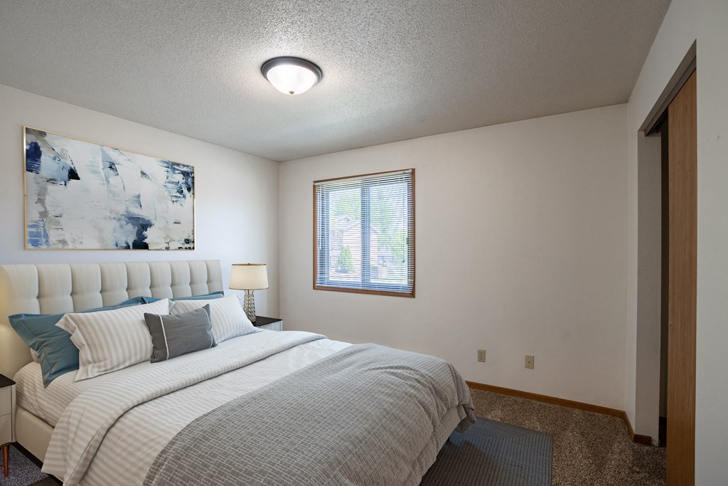 a bedroom with a bed and a window.Fargo, ND Southview Village Apartments