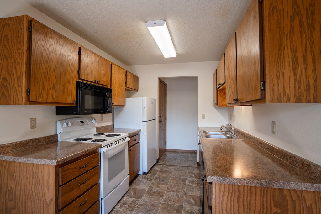 an empty kitchen with white appliances and wooden cabinets. Fargo, ND Southview Village Apartments