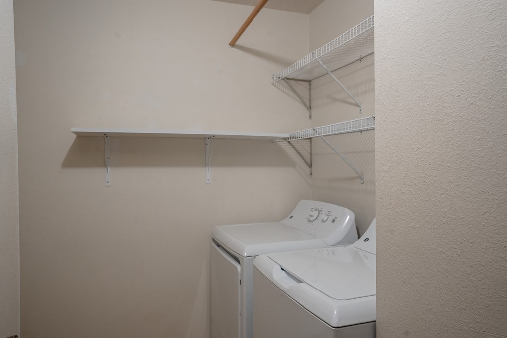 a washer and dryer in a laundry room with a shelf on the wall. Fargo, ND Southview Village Apartments