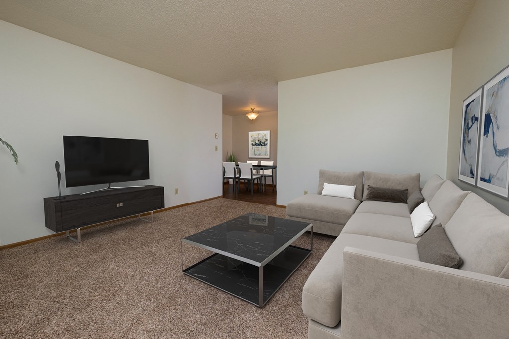 a living room with a couch, coffee table, and tv with the dining room in the background. Fargo, ND Southwind Apartment
