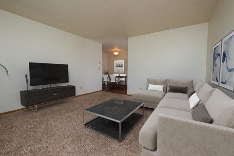 a living room with a couch, coffee table, and tv with the dining room in the background. Fargo, ND Southwind Apartment