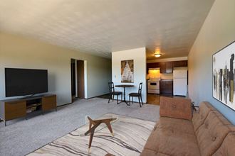 a living room with a couch and a tv and a kitchen with a table. Fargo, ND Spring Apartments