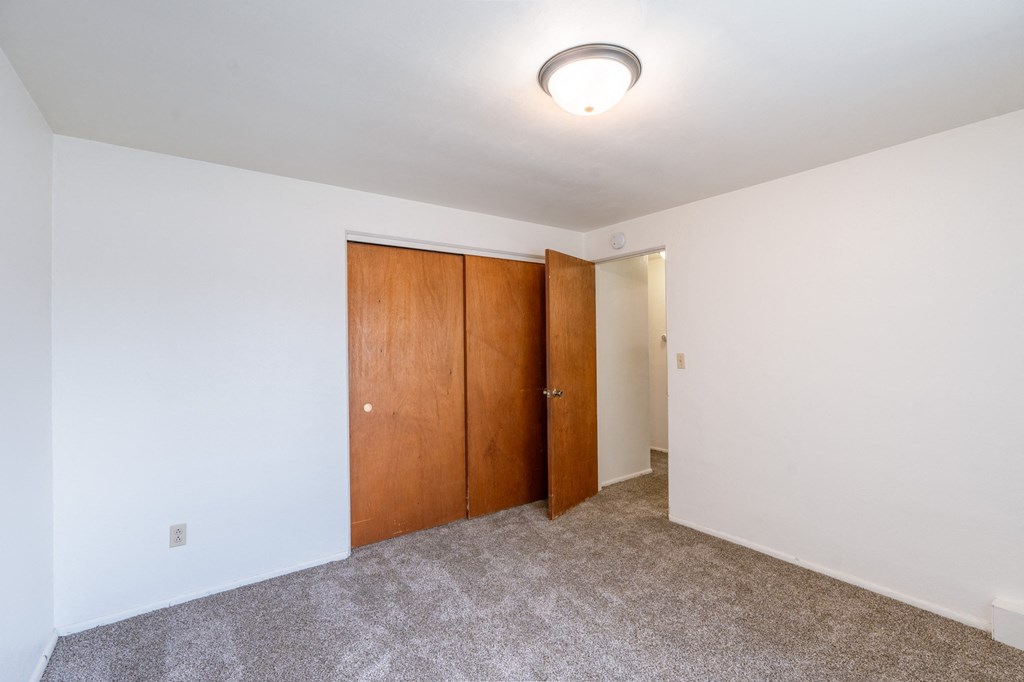 a room with a carpeted floor and a door to a closet. Fargo, ND Spring Apartments