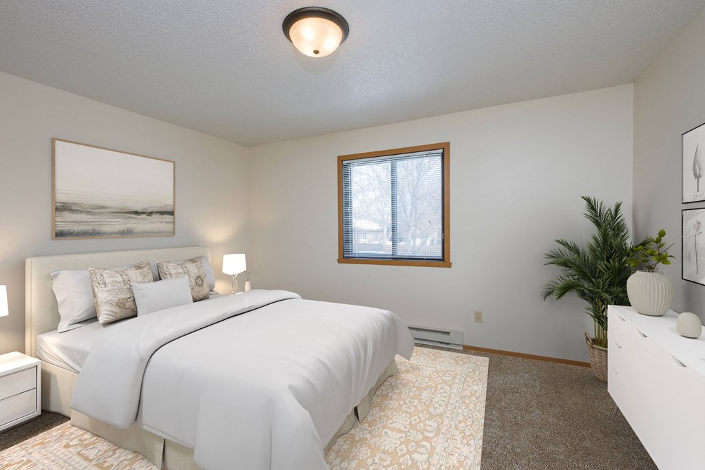 Fargo, ND Sugar plum apartments. A bedroom with a large white bed, white dresser, and white night stands with a lamp on each,  and window.