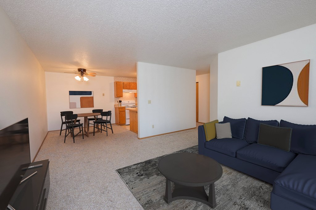 Fargo, ND Sugar Plum Apartments. A living room with a navy blue couch, a coffee table, and a dining area with a table and four chairs in the background.