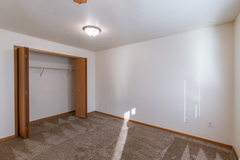 a bedroom area with a closet in a studio apartment.  Fargo, ND Sunwood Apartments  | Living and kitchen Fargo, ND Sunwood Apartments