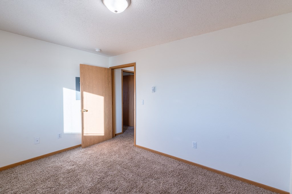 a bedroom with white walls and carpet.  Fargo, ND Sunwood Apartments  | Living and kitchen Fargo, ND Sunwood Apartments