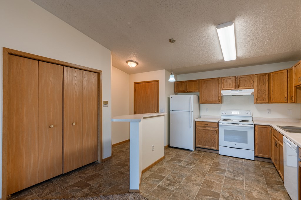 a kitchen with white appliances and wooden cabinets.  Fargo, ND Sunwood Apartments  | Living and kitchen Fargo, ND Sunwood Apartments