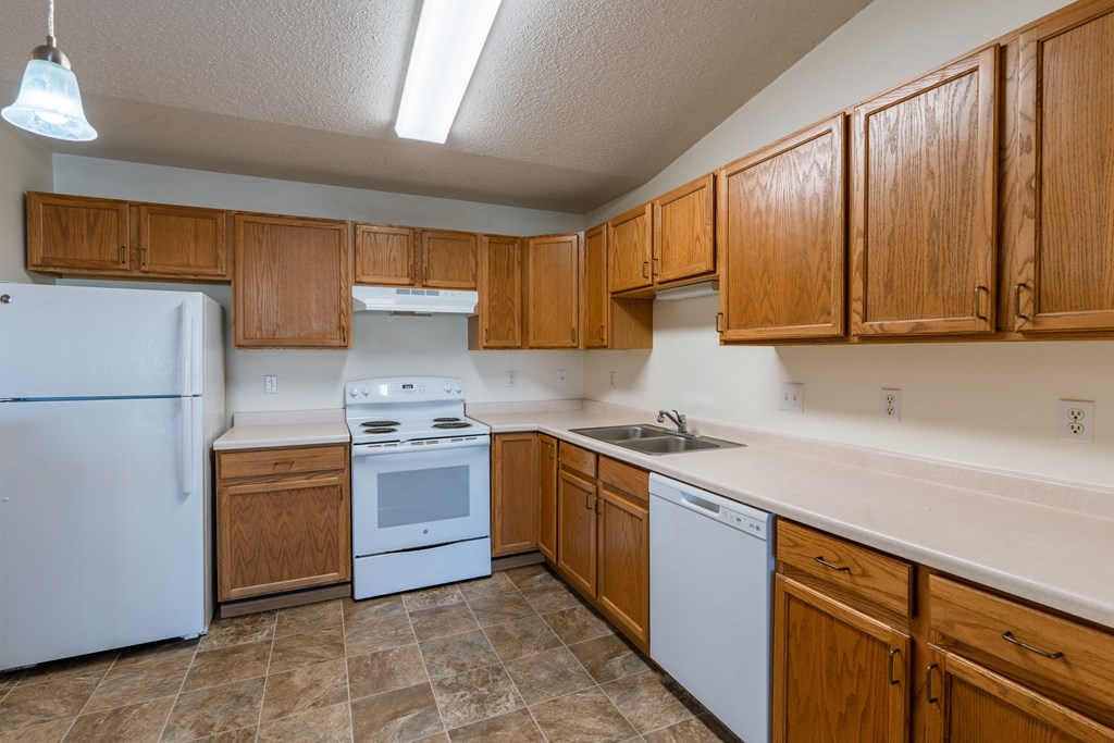 Fargo, ND Sunwood Apartments | Living and kitchen Fargo, ND Sunwood Apartments | Kitchen a kitchen with white appliances and wooden cabinets. Fargo, ND Sunwood Apartments | Living and kitchen Fargo, ND Sunwood Apartments