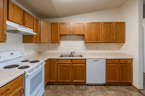 a kitchen with white appliances and wooden cabinets.  Fargo, ND Sunwood Apartments  | Living and kitchen Fargo, ND Sunwood Apartments