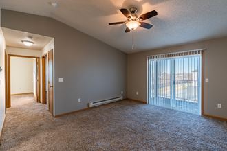 a living room with a ceiling fan and a glass sliding door with a hallway to the left.  Fargo, ND Sunwood Apartments  | Living and kitchen Fargo, ND Sunwood Apartments