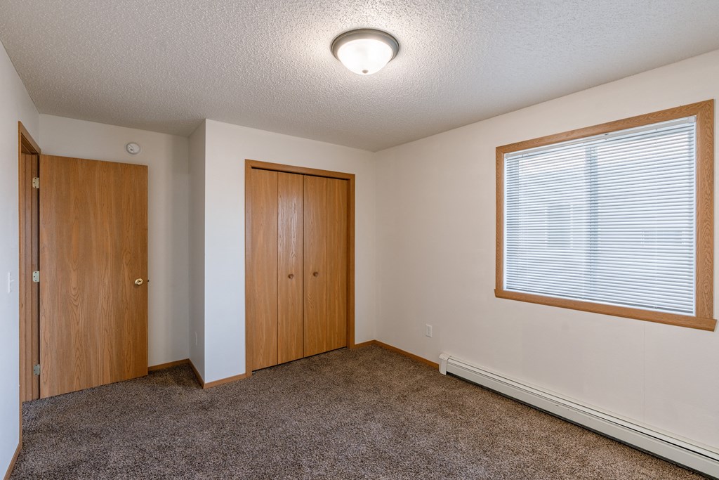 an empty living room with carpet and a door to a bedroom. Fargo, ND Thunder Creek Apartments