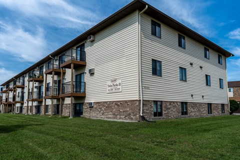 The exterior of a three level apartment building with a grass area out front