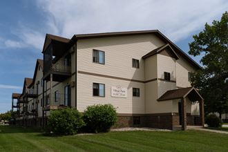 Fargo, ND Village Park Apartments. An exterior view of a large apartment building with a grassy area in front of it